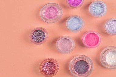 Kozmetik. Makyaj. Ufalanmış parlak gölgeleri, parıltılı kavanozları. Pembe, şeftali, bej arka planda altın renkler. Closeup. Metin veya tasarım alanı.