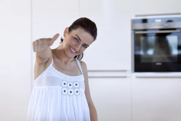 Donna posa e mano gesticolando pollice in alto segno in cucina — Foto Stock