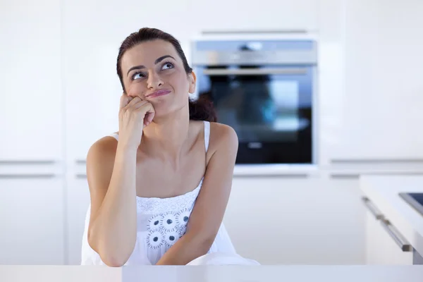 Portrait of a cheerful woman thinking at the kitchen counter — Stock Photo, Image