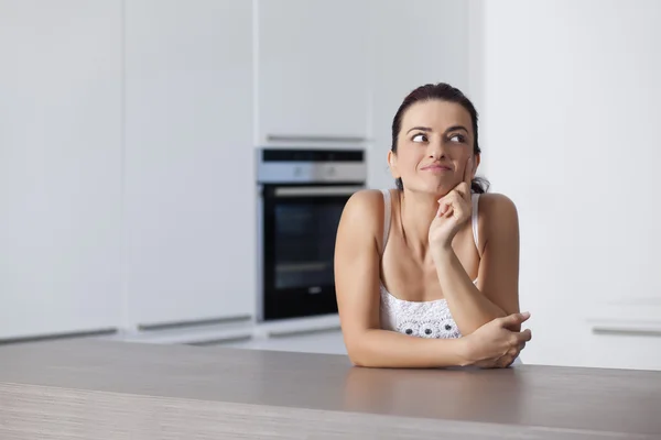 Portrait of a happy female thinking at the kitchen counter — Stock Photo, Image
