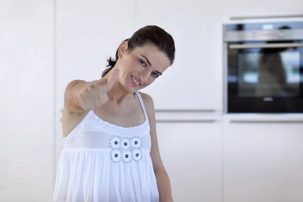 Donna posa e mano gesticolando pollice in alto segno in cucina — Foto Stock