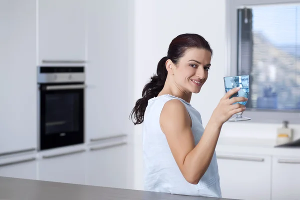 Retrato de uma mulher feliz segurando um copo na cozinha — Fotografia de Stock
