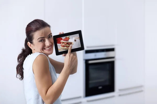 Young woman showing a digital tablet screen in the her kitchen — Stock Photo, Image