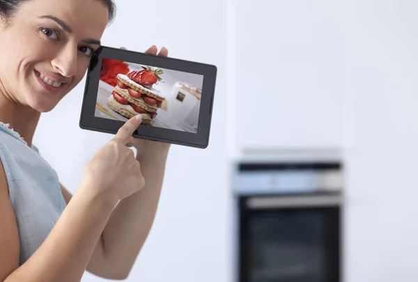 Young woman showing a digital tablet in the her kitchen — Stock Photo, Image