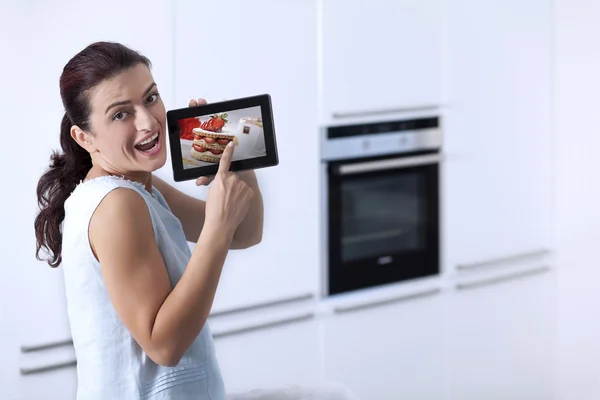Νεαρή γυναίκα που δείχνει μια ψηφιακή δισκίο σε το της κουζίνας — Φωτογραφία Αρχείου