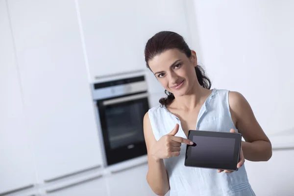 Young woman showing a digital tablet in the her kitchen — Stock Photo, Image
