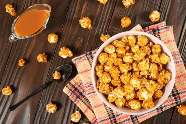 Clay bowl with caramel popcorn on wooden background flat lay