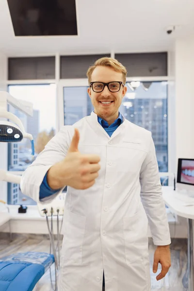 Uśmiechnięty Lekarz Dentysta Białym Płaszczu Pokazuje Kciuki Góry Patrzy Kamerę — Zdjęcie stockowe