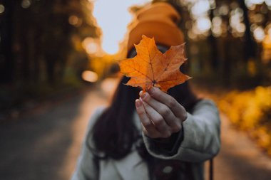 Genç bir kadın yüzüne bir akçaağaç yaprağı tutuyor.