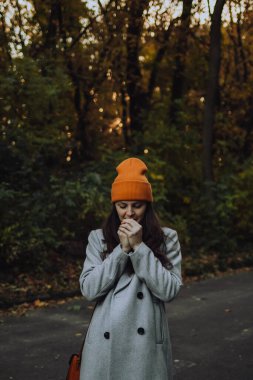 Dışarıda yün paltosuyla ellerine nefes alan genç bir kadın.