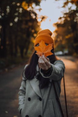 Genç bir kadın yüzüne bir akçaağaç yaprağı tutuyor.