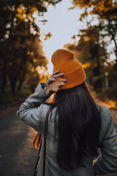 Genç bir kız akşamleyin sokağın ortasında tek başına elinde akçaağaç yaprağı ve güneş ışınlarıyla dikiliyor.