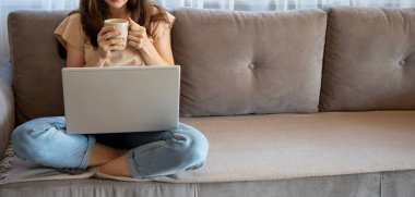 Genç bir bayanın bayrağı evde çalışırken bir fincan kahve içiyor. Bir kız düşünüyor ve bir dizüstü bilgisayarla koltukta oturuyor.