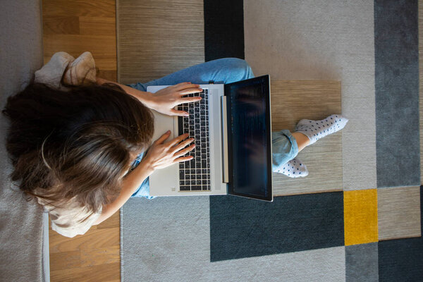 View from above of woman working on a laptop while sitting on the floor. A young girl is programming