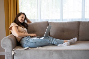 Mutlu bir kadın uzaktan bilgisayarla çalışırken gülümsüyor. Konforlu ve şık bir dairede rahat bir iş. 