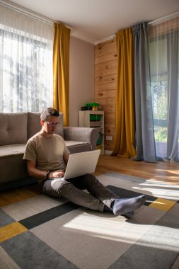 Gündelik elbiseli bir adam güneşli bir dairede yerde çalışıyor.