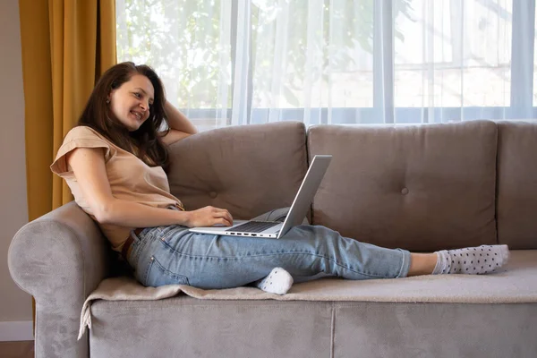 En kvinna ler när hon pratar med någon på distans. Flicka som arbetar hemifrån — Stockfoto