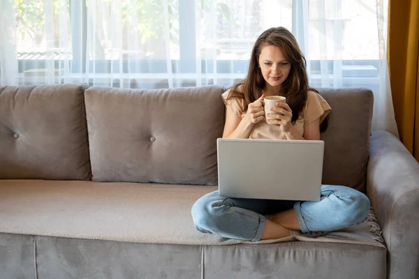 En ung kvinna dricker en kopp kaffe när hon arbetar hemifrån.. — Stockfoto