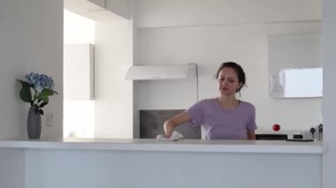 Genç bir kadın mutfak yüzeyini temizliyor ve telefon bildirimi ile yarıda kesiyor.. 