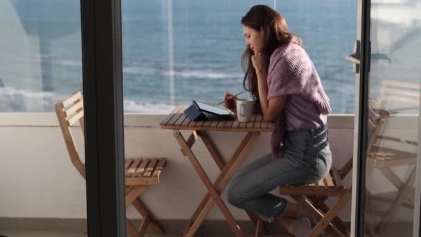 テラスにスタイラス付きのデジタルタブレットで作業女性の側のビュー お茶を飲み 海を見て — ストック動画