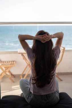 Balkonun yanındaki kanepede oturan genç bir kadın el ele tutuşup denize bakıyor.