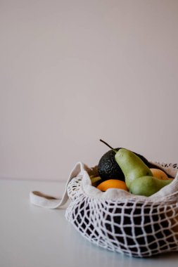 Çevreye duyarlı bir çantada çeşitli meyveler masanın üzerinde yatıyor. Fotokopi alanı olan sağlıklı bir daire. Avokado, limon, şeftali, armut, portakal.