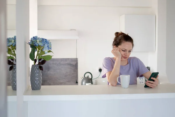 Bored Woman Using Her Phone Kitchen Drinking Her Tea Morning — Stock Photo, Image