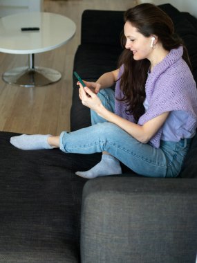 Kulaklıklı genç bir kadın akıllı telefonuyla müzik dinliyor..