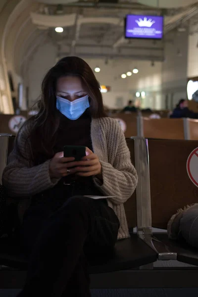 Скучающая молодая женщина сидит в аэропорту и смотрит в телефон — стоковое фото