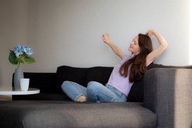 Genç bir kadın balkonun yanındaki kanepede oturuyor ve sabahları esniyor.