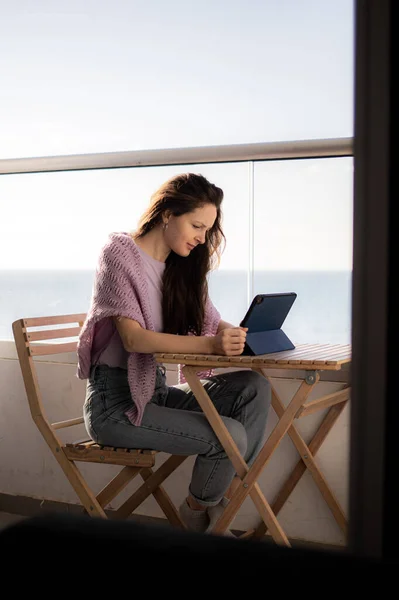 Genç bir kadın deniz kenarındaki balkondaki tablette yazı yazıyor. — Stok fotoğraf