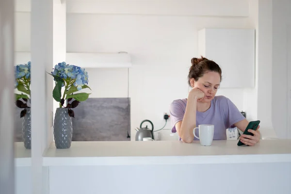 Bored Woman Using Her Phone Kitchen Drinking Her Tea Morning — Stock Photo, Image
