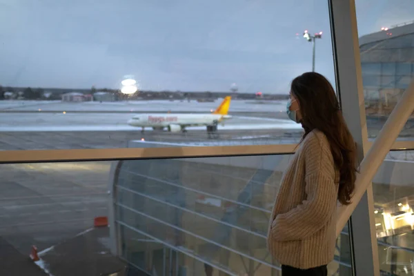 空港ターミナルの窓の近くに白人女性が立っていて 飛行機を見ている 女の子は搭乗を待っています — ストック写真