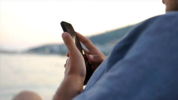 Gros plan du jeune homme utilise son smartphone tout en étant assis à la plage — Video