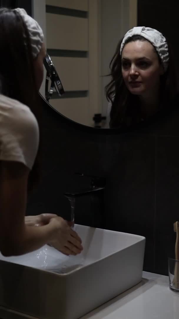 Pionowe nagranie kobiety w opasce czyszczącej twarz przed lustrem — Wideo stockowe