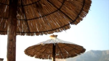 Gün batımında saman şemsiyeli ve güneşli boş bir kumsalın hareket videosu.
