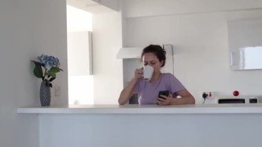 Genç bir kadının mutfakta telefonunu kullanıp çayını içmesinin sabah rutini.
