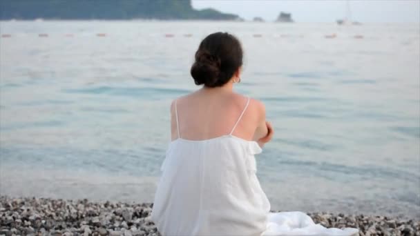 Mujer Joven Vestido Blanco Sentada Sola Playa Mirando Mar Tiempo — Vídeos de Stock