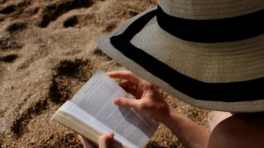 Kumsalda kitap okuyan güneş şapkalı bir kadının videosu.. 
