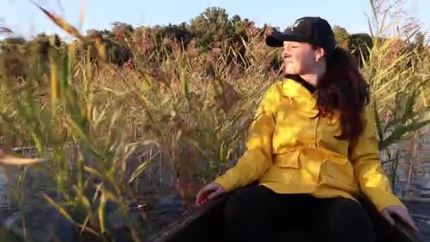 Lächelnde junge Frau sitzt auf einem Boot im See und segelt zwischen Wasserpflanzen — Stockvideo