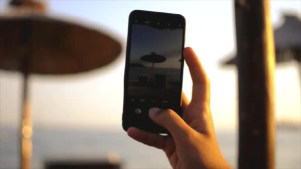 L'homme prend une photo d'un parasol en paille avec des chaises longues en utilisant un téléphone mobile — Video