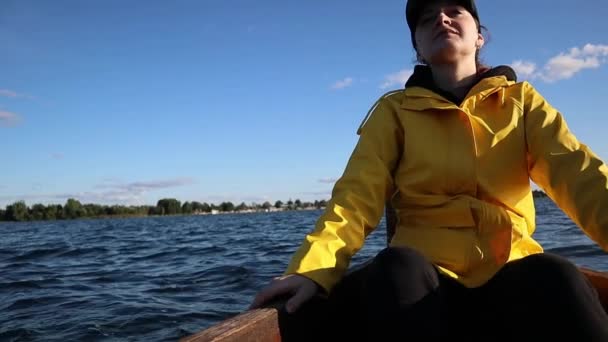 Mujer joven en impermeable amarillo y gorra sentada en un barco y mirando hacia el exterior — Vídeo de stock