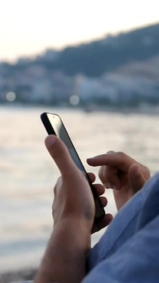 Gros plan du jeune homme utilise son smartphone tout en étant assis à la plage — Video