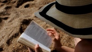 Yaz şapkalı kadın sahilde kitap okuyor.