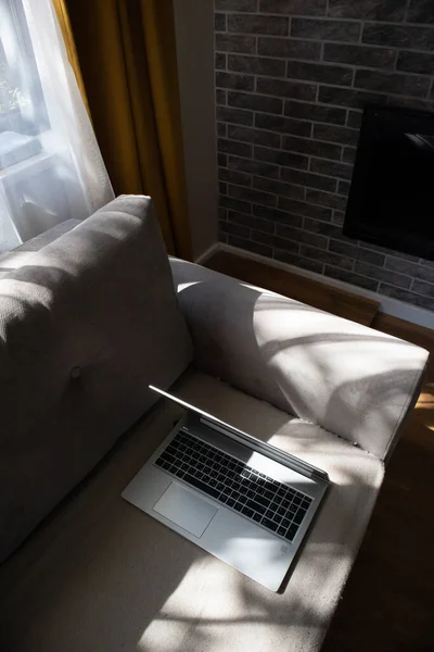 阳光灿烂的一天 一台打开的笔记本电脑躺在沙发上 漂亮的现代内部 没有人的概念 — 图库照片