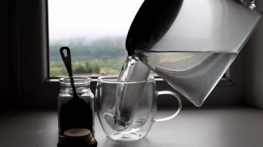 Bir insan şeffaf çaydanlıktan cam bardağa su dökerek çay yapıyor.. 