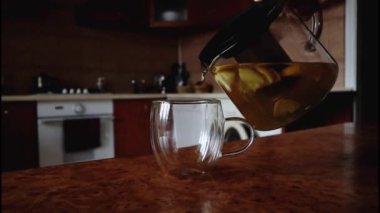 Birisi ev mutfağındaki çaydanlığın bardağına limon ve zencefilli sağlıklı çay döküyor.