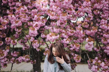 Esmer genç bir kadın ilkbaharda büyük bir sakura ağacının önünde duruyor.