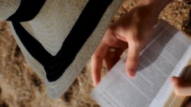 Kumsalda kitap okuyan yaz şapkalı bir kadının dikey videosu.. 