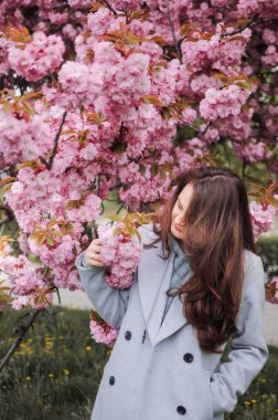 Esmer genç bir kadın ilkbaharda büyük bir sakura ağacının önünde duruyor.
